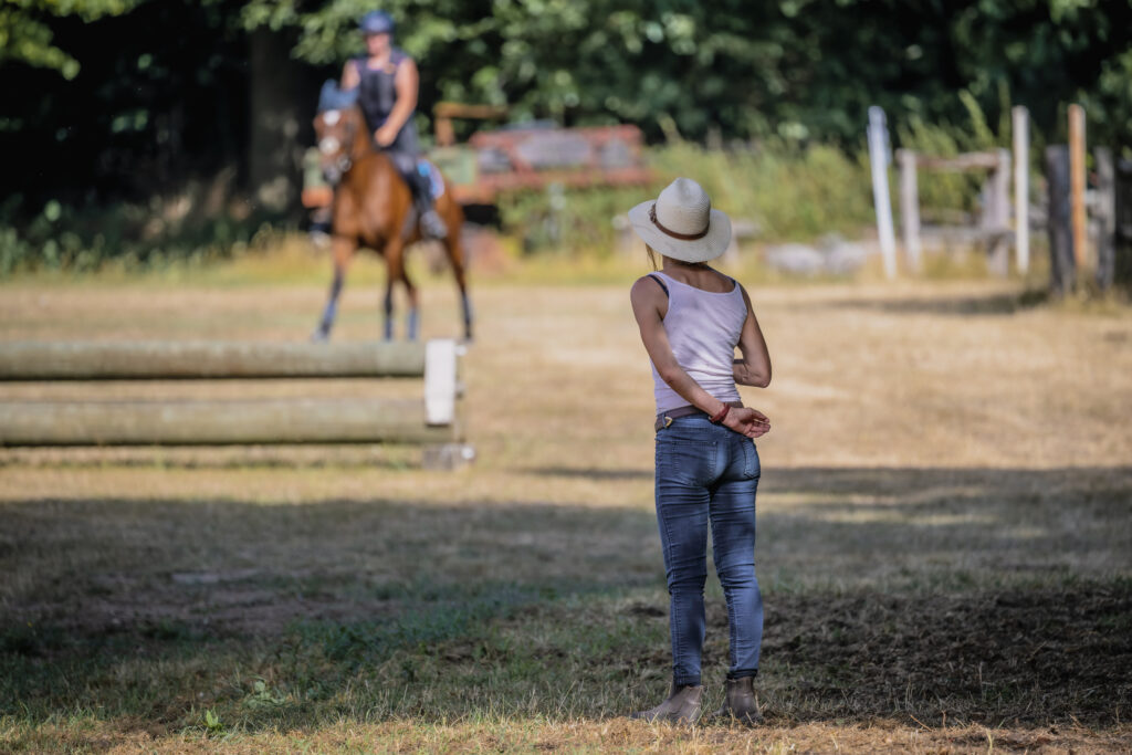 Trainerin beobachtet Reiterin auf einem Pferd beim Geländetraining.